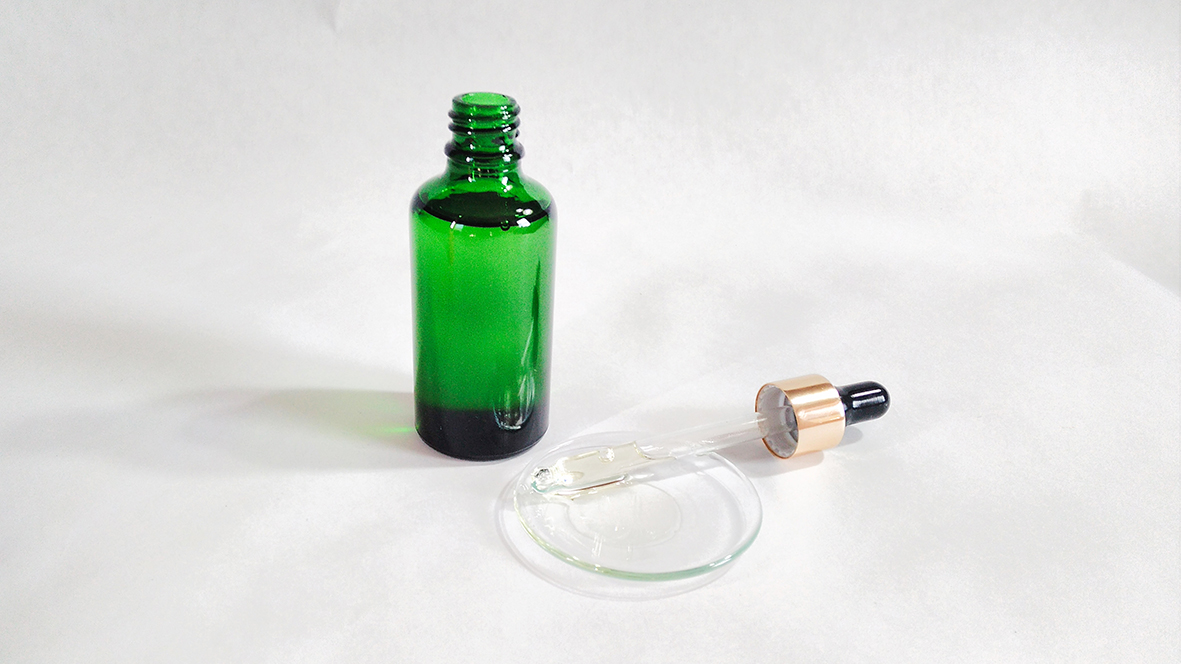 Mentolový masážny olej v zelenej sklaenenj fľaške na bielom pozdí s kvapátkom a olejom.